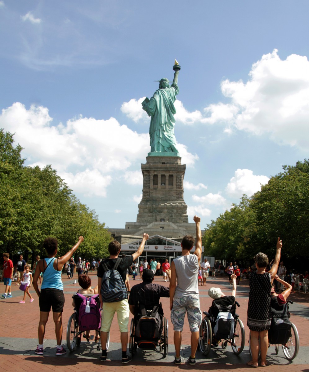 A group of people standing and  in wheel chairs in front of the Statue of Liberty